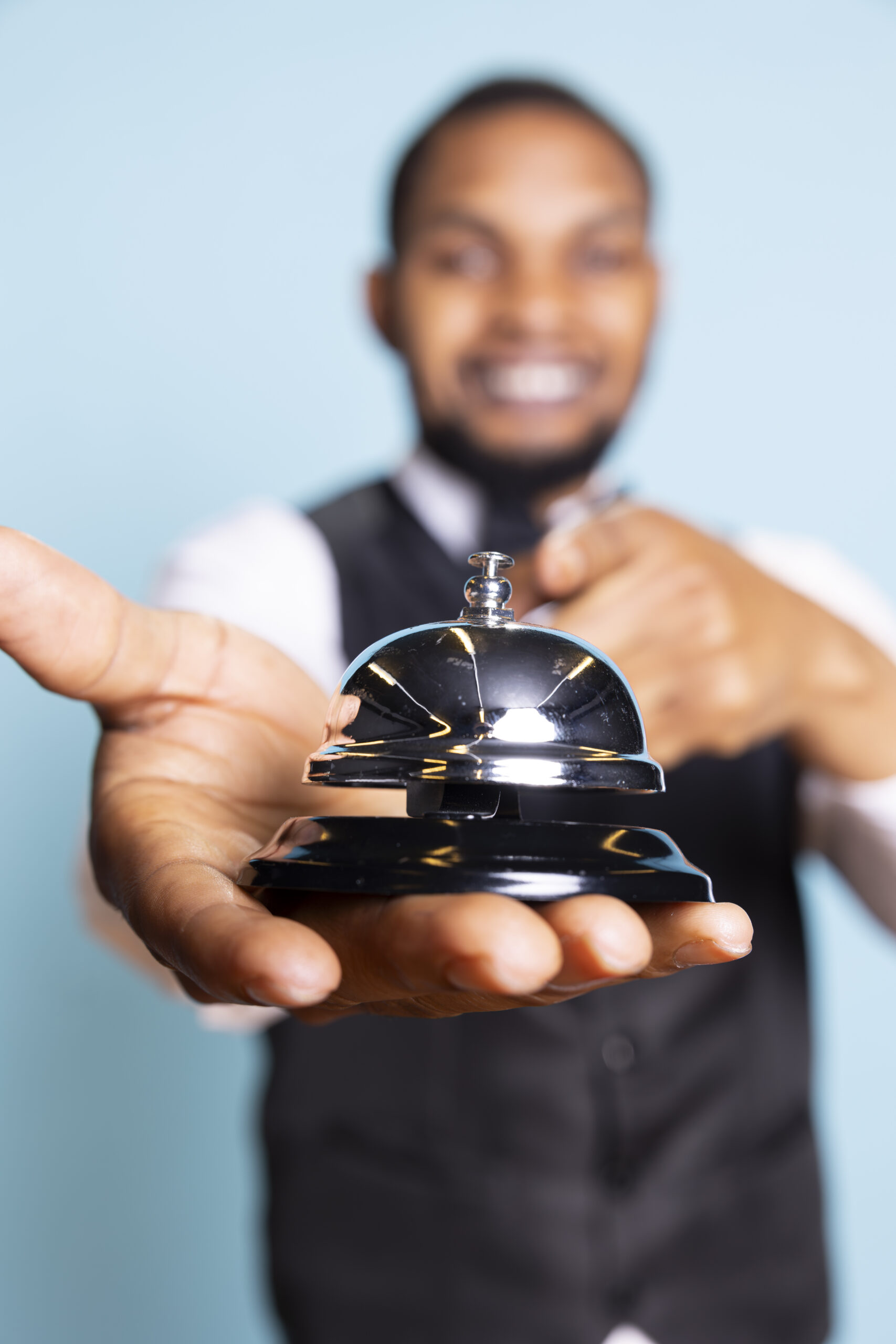 Bellhop doorkeeper ringing the service bell to present his help and assistance upon the guests arrival against blue background. Hotel porter providing great luxury services at resort.